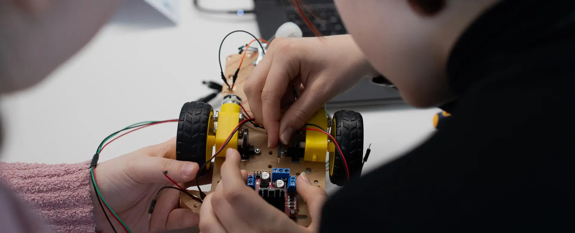 Schülerin & Schüler arbeiten an einem Roboter-Fahrzeug, Laptop auf dem Tisch