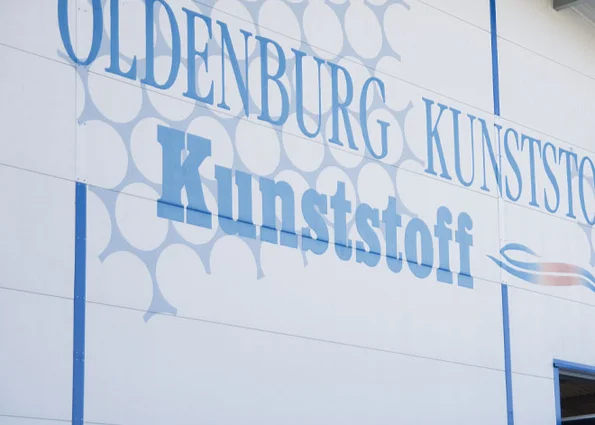 Production plant I of OLDENBURG KUNSTSTOFF-TECHNIK GmbH in Chieming/Bavaria Hall front facade with blue lettering ‘OLDENBURG KUNSTSTOFF’ and graphic circular areas