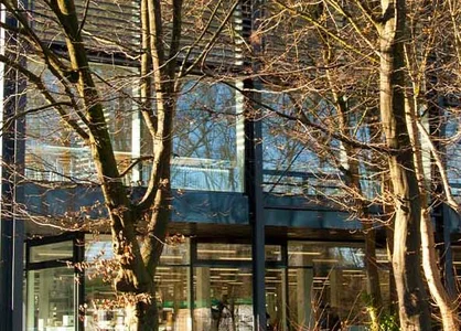 Modernes Gebäude mit großen Glasfassaden, umgeben von kahlen Bäumen an einem sonnigen Herbsttag.
