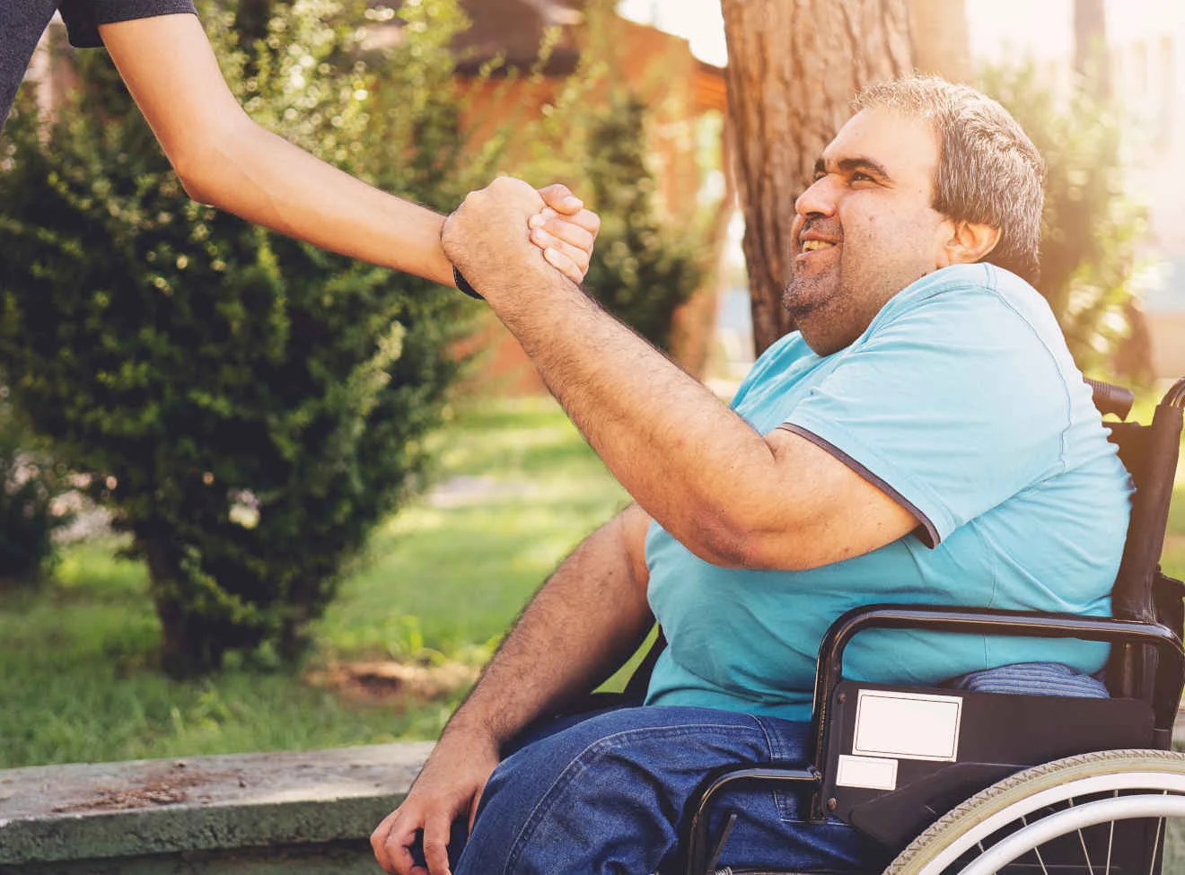 Unterstützung und Teilhabe für Menschen mit Behinderung in der Evangelischen Stiftung Neuerkerode Mann im Rollstuhl begrüßt im Park eine stehende Person mit einem Händedruck.