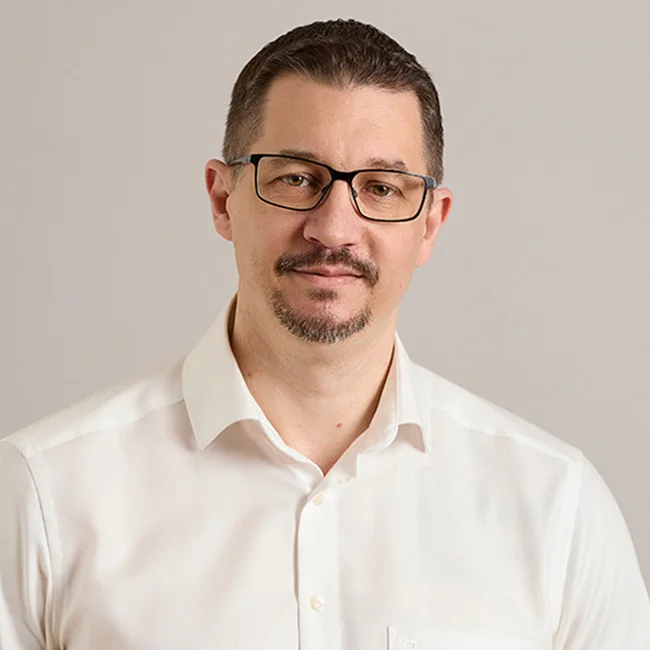 Marcus Hennig – IT-Leiter beim ACV Porträt eines dunkelhaarigen Mannes mit Brille im weißen Hemd vor neutralem Hintergrund.