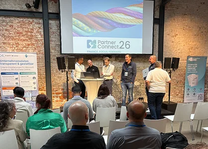 Personen verfolgen auf der PartnerConnect26 eine Präsentation vor Backsteinwand.