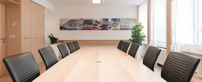 Moderner Konferenzraum mit großem Holztisch, schwarzen Lederstühlen, Pflanzen & abstraktem Wandbild