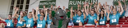 Das GOB-Team jubelt auf der Tribüne der Galopprennbahn neben dem RUN & FUN-Maskottchen