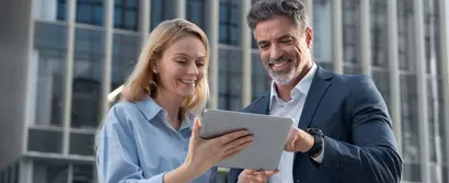 Lächelnde Geschäftspersonen schauen sich gemeinsam Inhalte auf einem Tablet vor Bürogebäuden an.