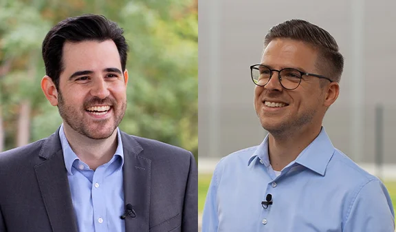 Zwei lächelnde Personen im Business-Outfit, nebeneinander im Freien; Porträts vor Naturhintergrund.