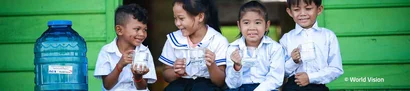 Echtstart bei World Vision Deutschland e. V. | unitop Fundraising | 1905 x 425 Pixel Vier lachende Kinder auf grüner Holztreppe mit Wasser in der Hand, links ein Wasserbehälter