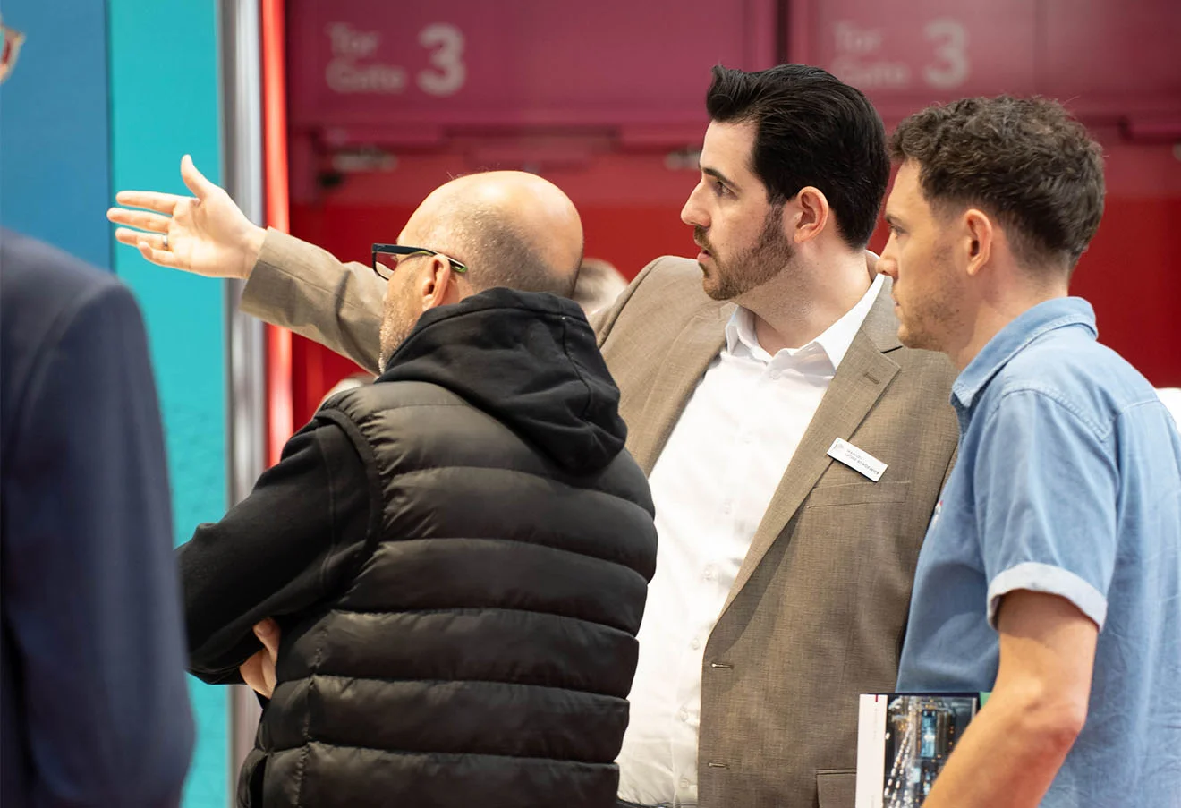 Drei Personen am GOB-Stand der LogiMAT 2026; Mitarbeiter zeigt auf Präsentationsfläche am Stand.