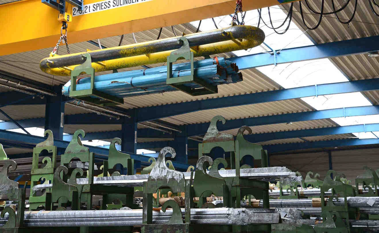 Krananlage im Einsatz bei STAHL KREBS Halle mit gelber Krananlage; gehobenes Bündel Stahlstäbe, darunter grüne Lagergestelle