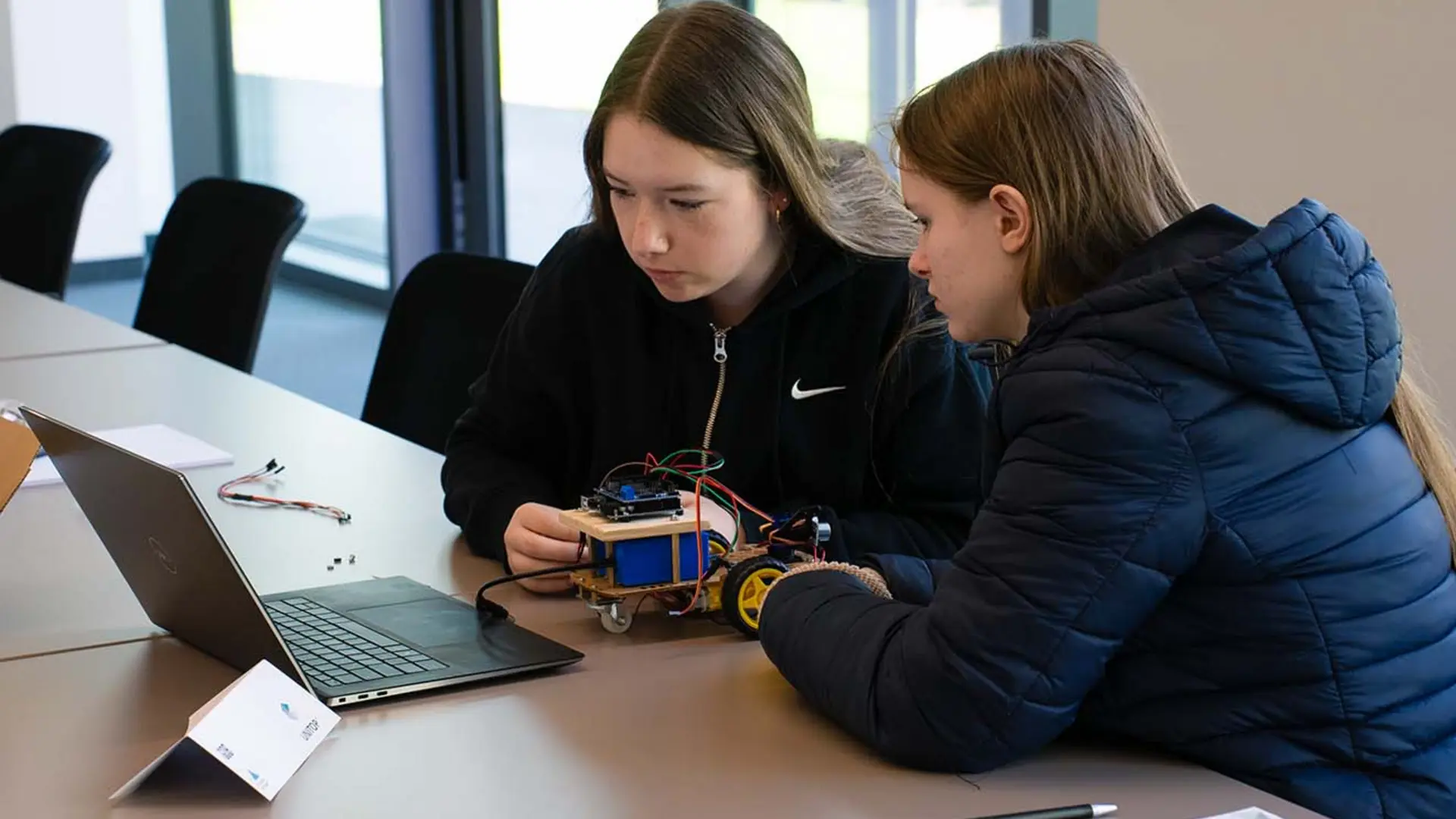 Zwei Teilnehmerinnen des Girls'Day 2025 programmieren einen Arduino-Roboter gemeinsam am Laptop.