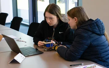 Zwei Teilnehmerinnen des Girls'Day 2025 programmieren einen Arduino-Roboter gemeinsam am Laptop.