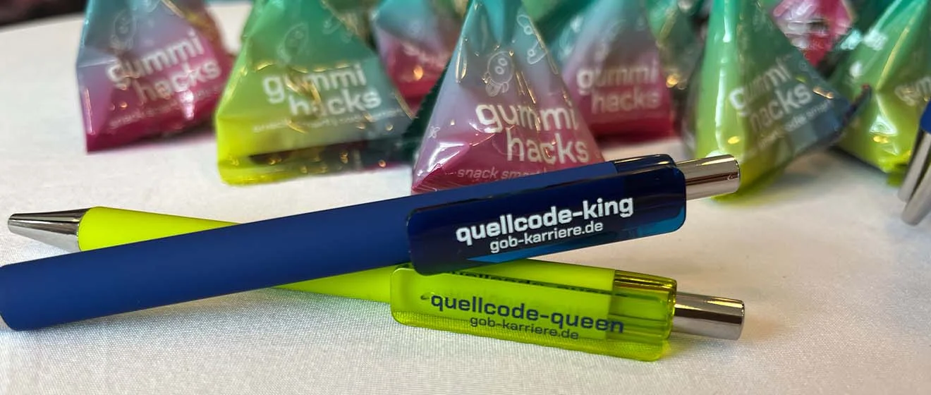 Give-aways für Quellcode-Kings und -Queens GOB-Kugelschreiber mit Aufdruck „quellcode-king“ und „quellcode-queen“ zwischen bunten süßen Snacks