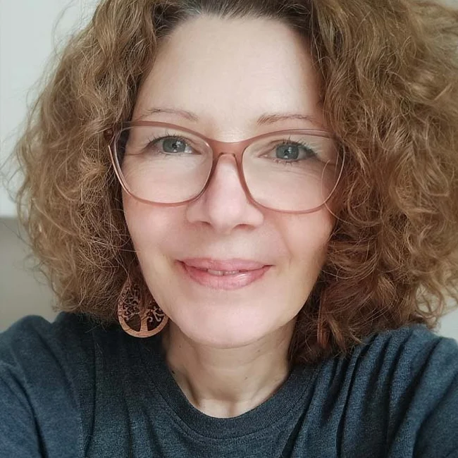 Nicole Förstl, Spendenservice-Expertin, World Vision Deutschland e. V. Frau mit lockigen Haaren und großer Brille lächelt in die Kamera vor hellem Hintergrund.