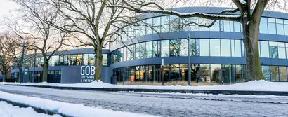 GOB-Gebäude im Winter, umgeben von schneebedeckten Bäumen und Straßen.