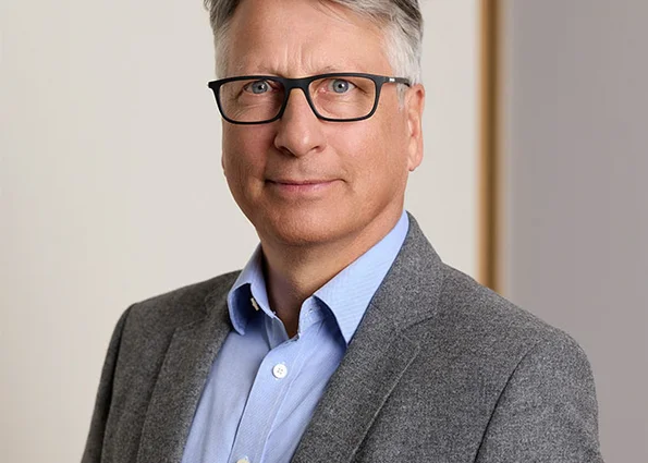 Porträt eines Mannes mit Brille im grauen Sakko vor hellem Hintergrund.