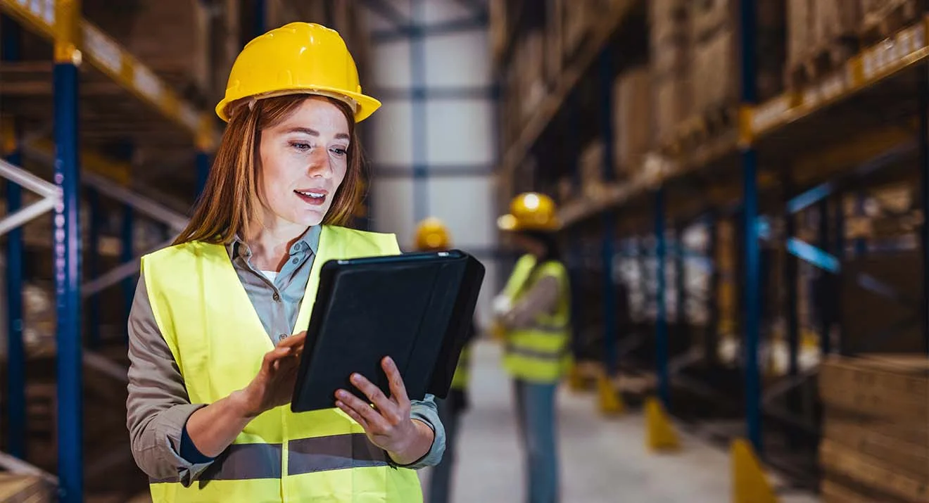 Frau mit Tablet überwacht die Abläufe im Lager – Beispiel für den Einsatz eines WMS.