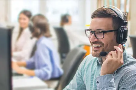 Lächelnder Kundenservice-Mitarbeiter mit Headset, der in einem lebhaften Büro Kunden betreut