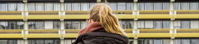 Dunkelblonde Studentin mit Rucksack vor RUB-Gebäude, von hinten aufgenommen