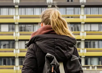 Dunkelblonde Studentin mit Rucksack vor RUB-Gebäude, von hinten aufgenommen.