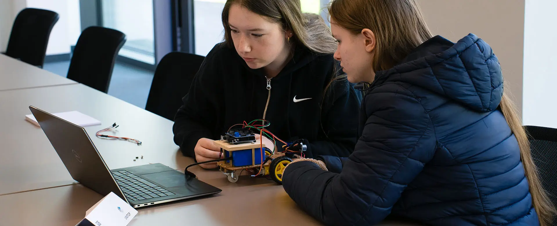 Zwei Teilnehmerinnen des Girls'Day 2025 programmieren einen Arduino-Roboter gemeinsam am Laptop.