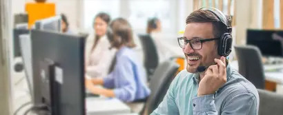 Smiling male customer service representative wearing a headset, assisting clients in a busy office.