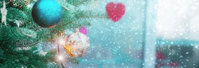 Weihnachtsbaum mit Kugeln und rotem Herzanhänger, davor sanft fallender Schnee.