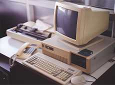 Desk with analogue corded telephone, fax machine, keyboard, cable mouse and computer tube monitor