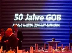 Schriftzug 50 Jahre GOB projiziert in weiß auf blauer Leinwand vor festlich gedecktem Tisch